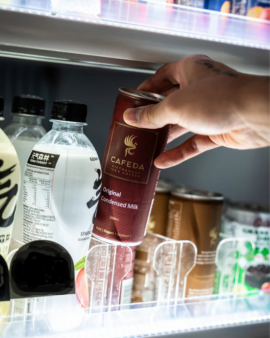 Hands holding Cafeda Vietnamese iced coffee cans alongside fresh baguette sandwiches, showcasing pre