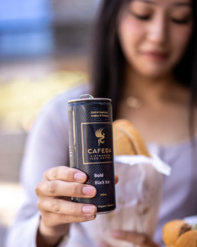 Hands holding Cafeda Vietnamese iced coffee cans alongside fresh baguette sandwiches, showcasing pre