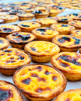 Portuguese custard tarts with golden flaky pastry and caramelised tops, served with cinnamon sticks,