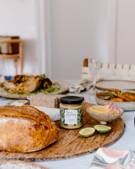 Hand holding Tall Poppy Gourmet Classic Spicy Tomato Relish jar beside sliced tomatoes and cucumber