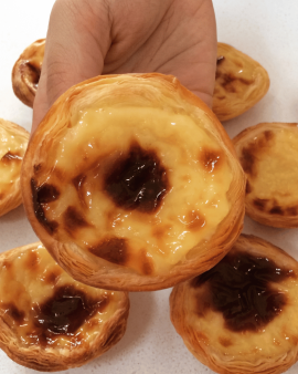Portuguese custard tarts with golden flaky pastry and caramelised tops, served with cinnamon sticks,